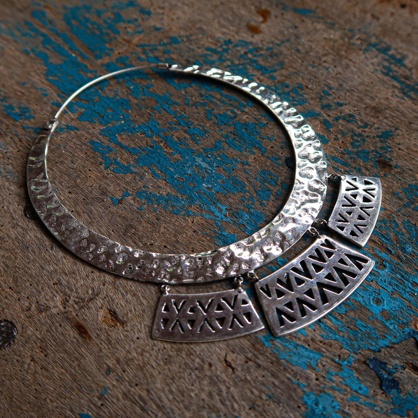 Sterling silver Olteca earring placed on a weathered blue-painted wooden background, highlighting their delicate craftsmanship.