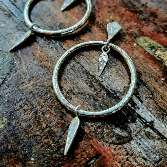 Sterling silver-plated circular earrings with a hammered texture, adorned with two elongated pendants suspended from the hoop on a vintage wood background.