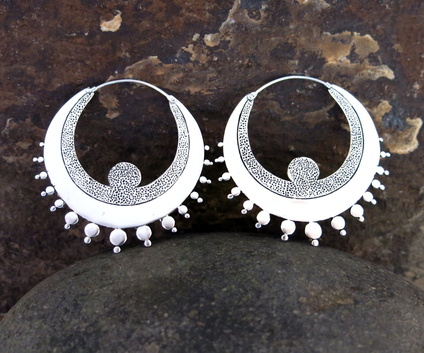 Crescent-shaped hoop earrings in silver-plated brass with textured detailing and sterling silver hooks.
