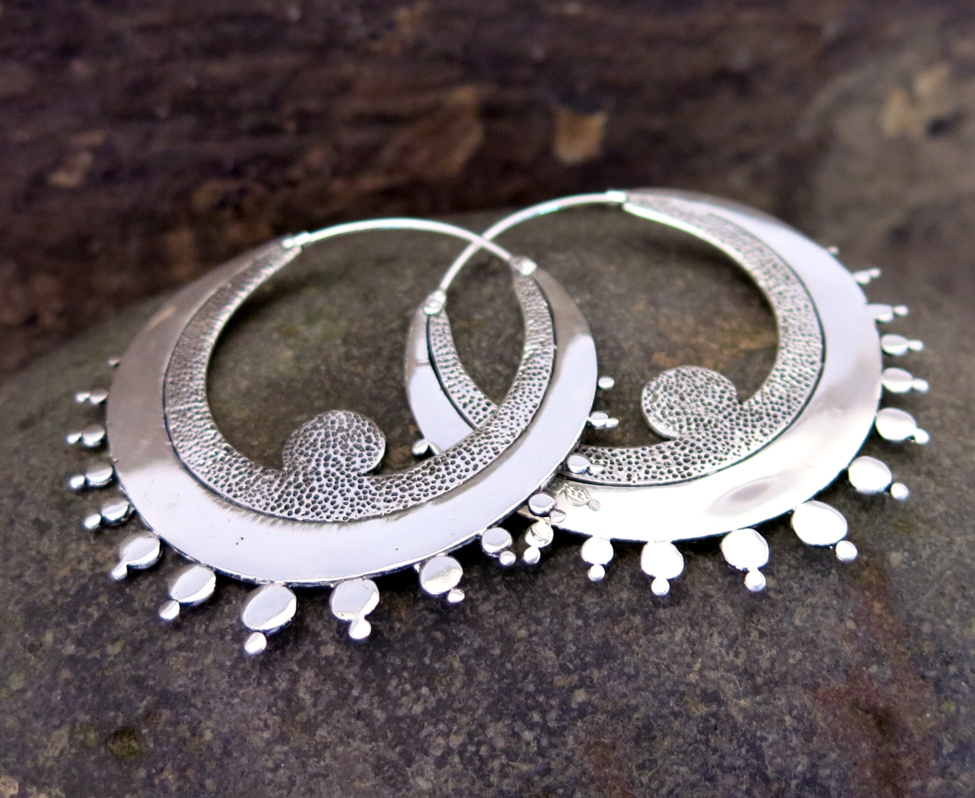 Crescent-shaped hoop earrings in silver-plated brass with textured detailing and sterling silver hooks.
