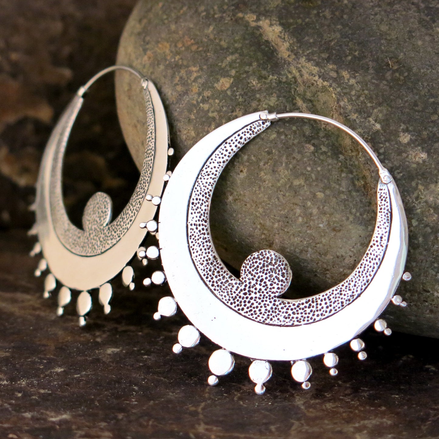 Crescent-shaped hoop earrings in silver-plated brass with textured detailing and sterling silver hooks.
