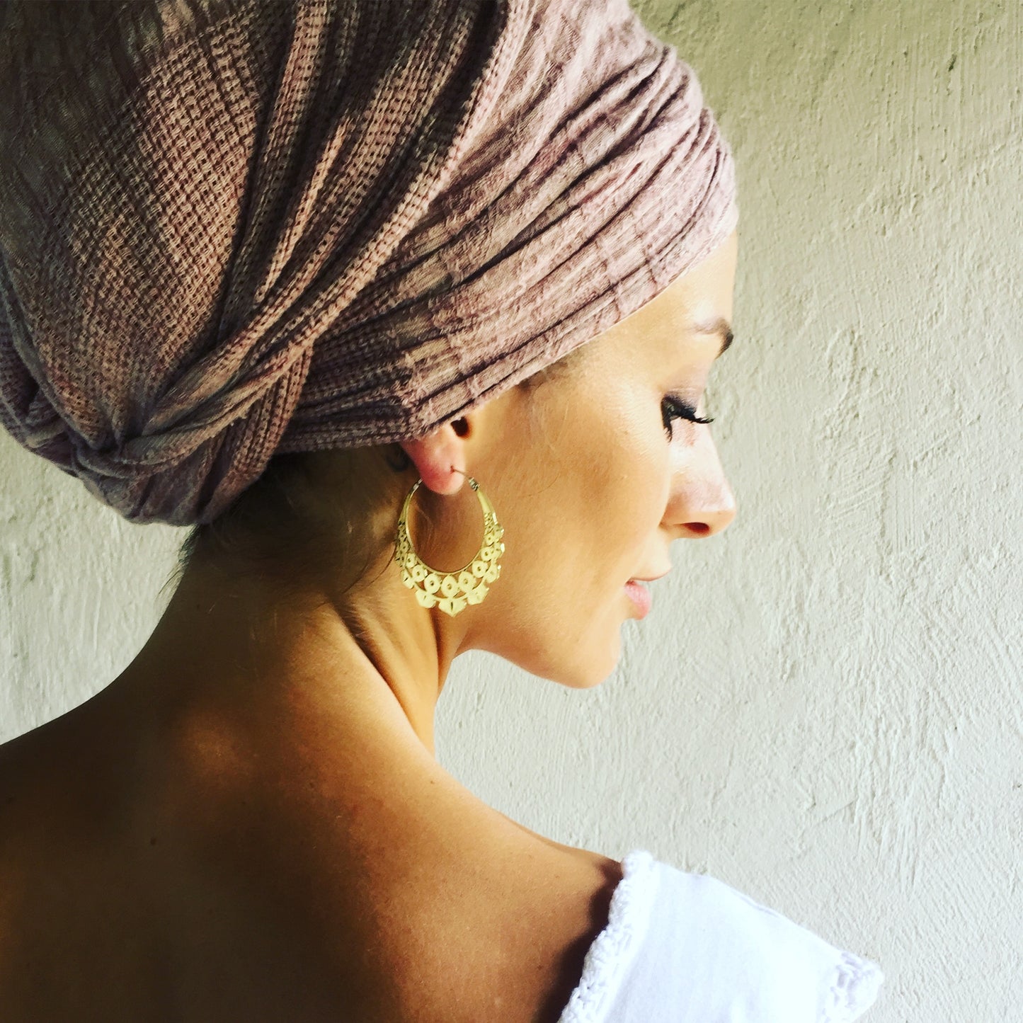 A model wearing the Italian brass Lotus Geo earrings, showcasing their lightweight, geometric lotus-inspired design in a warm, earthy setting.