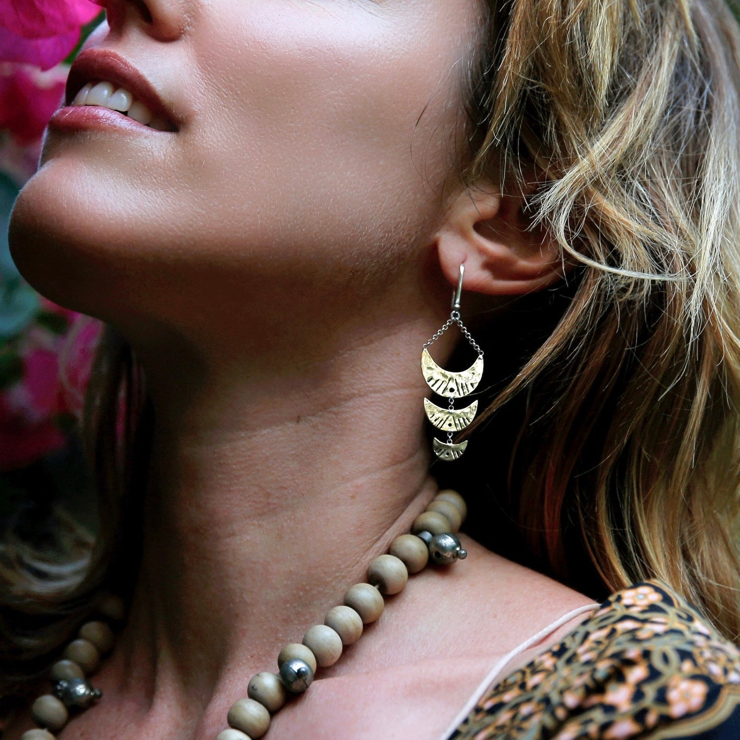 Close up of woman wearing Italian brass Berber Earrings with cascading crescent moon shapes, photographed in natural light against vibrant flowers.