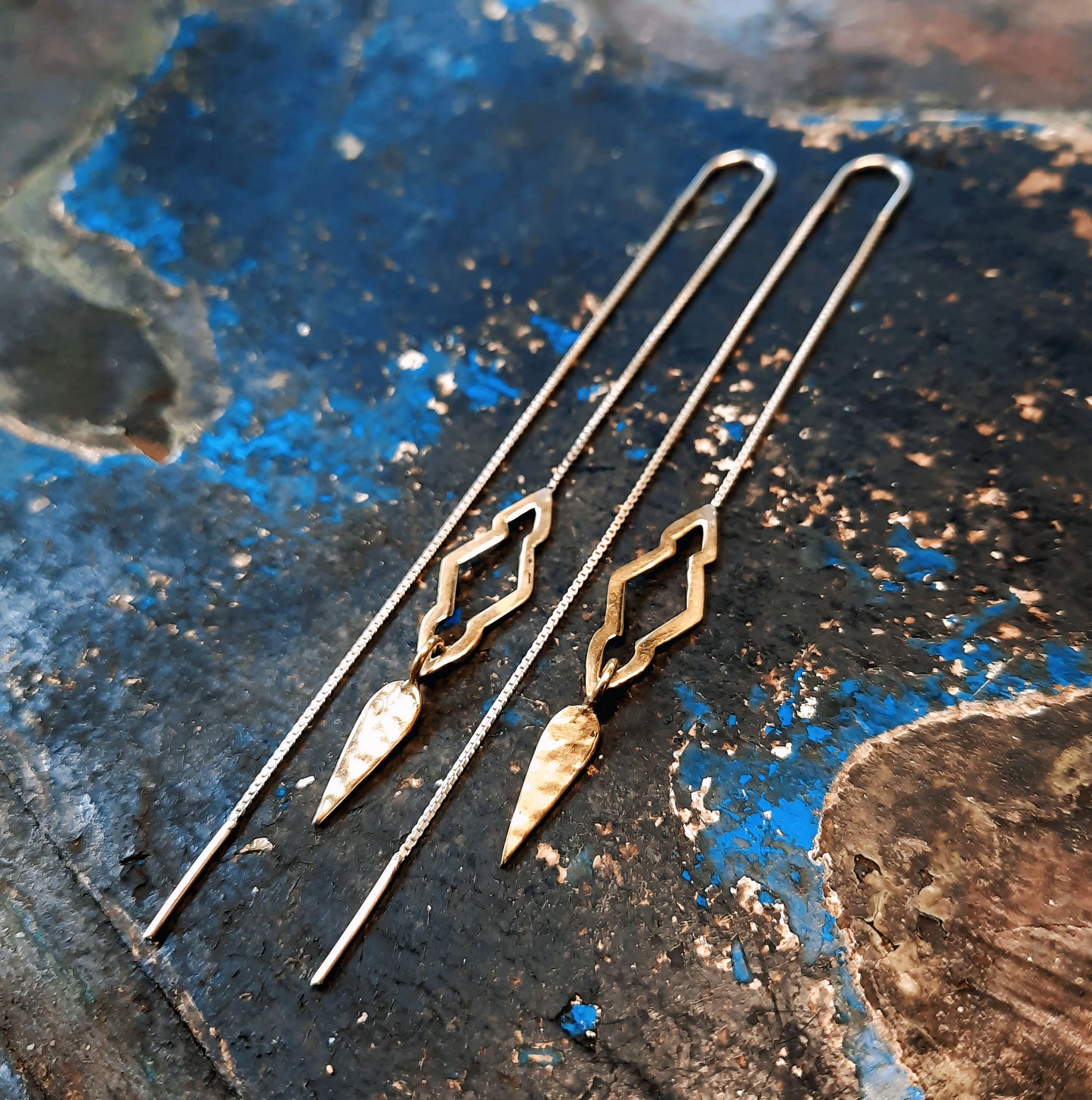 Close-up of Mali threader earrings in Italian brass, resting on a rustic wooden surface.
