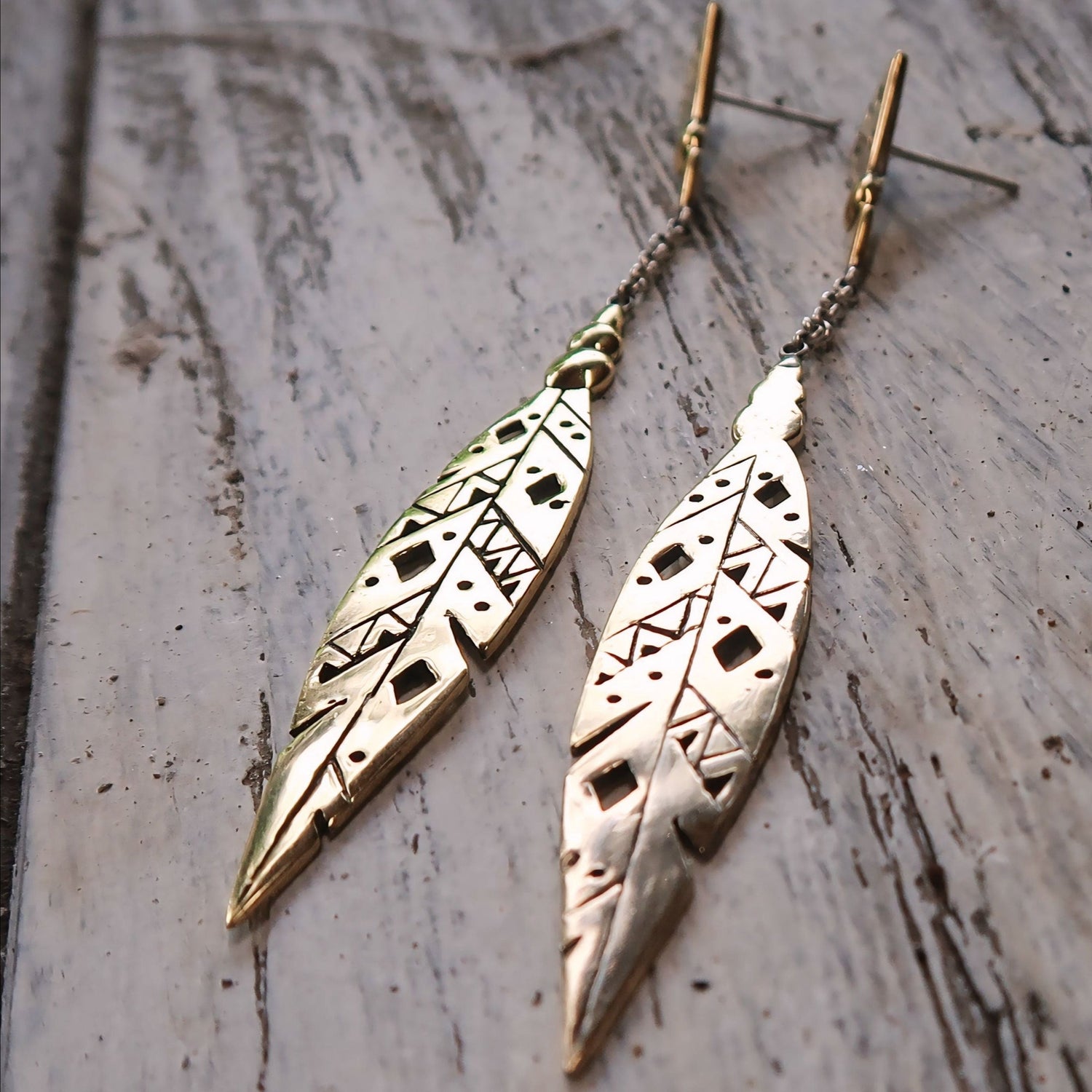 Close-up of Khiki earrings in Italian brass, highlighting intricate feather patterns and a delicate chain.