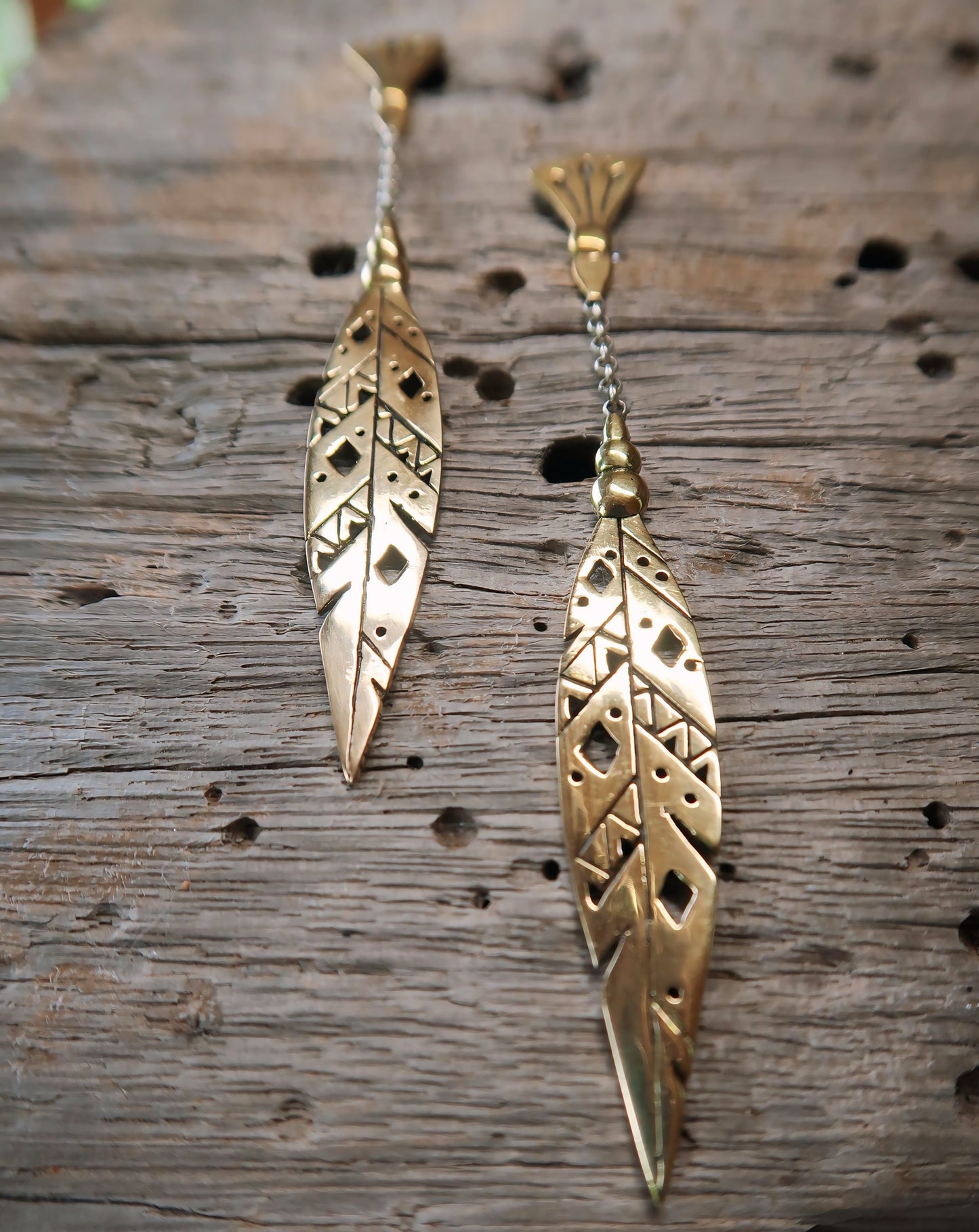 Close-up of Khiki earrings in Italian brass, highlighting intricate feather patterns and a delicate chain.