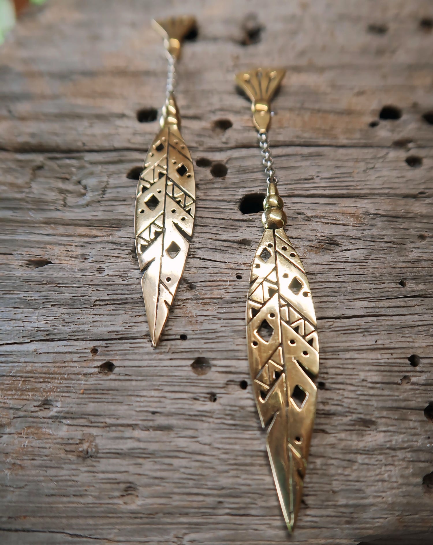 Close-up of Khiki earrings in Italian brass, highlighting intricate feather patterns and a delicate chain.