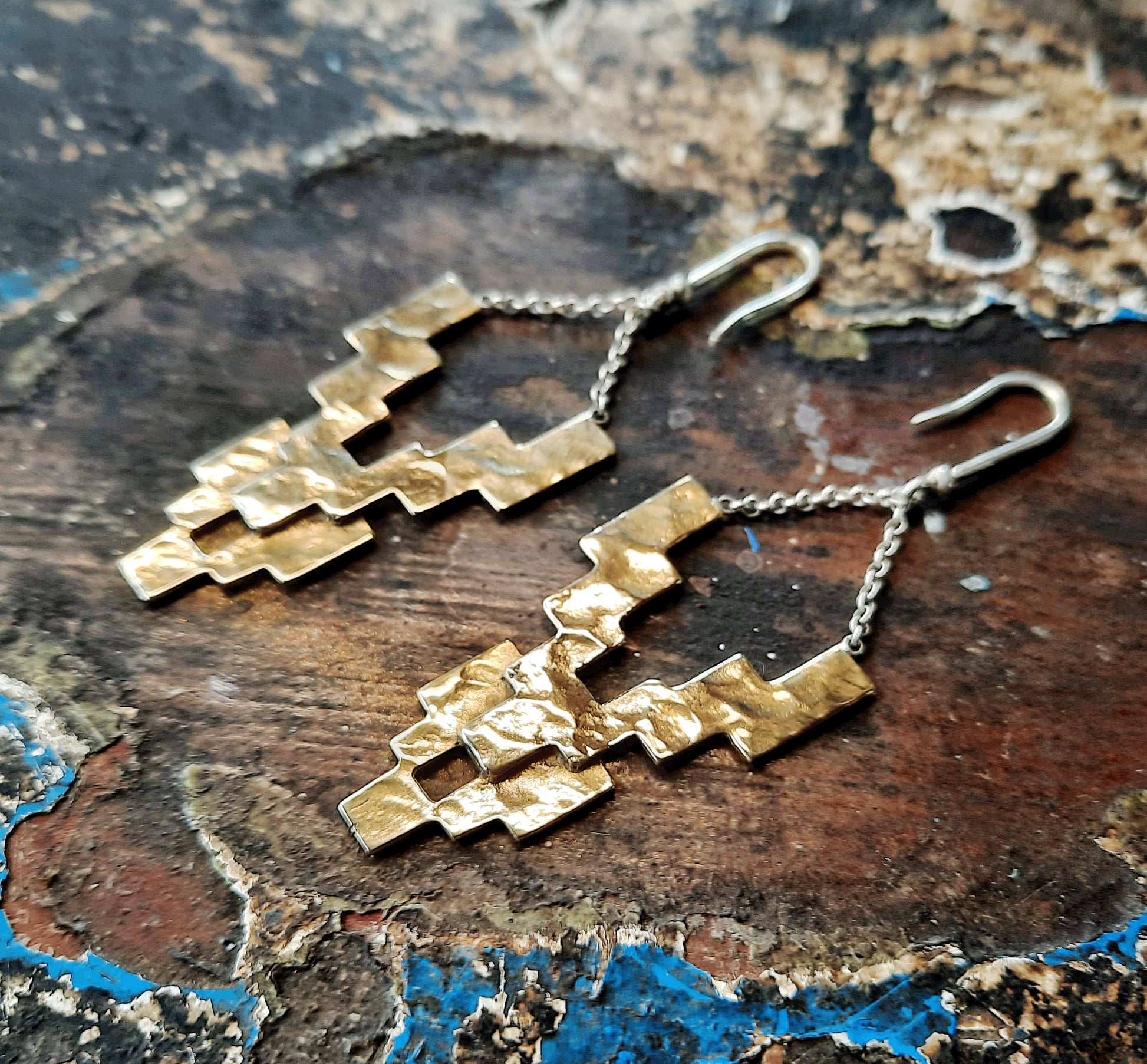 Close-up of the Nuba earrings in warm gold toned brass, highlighting their layered geometric design and textured finish.
