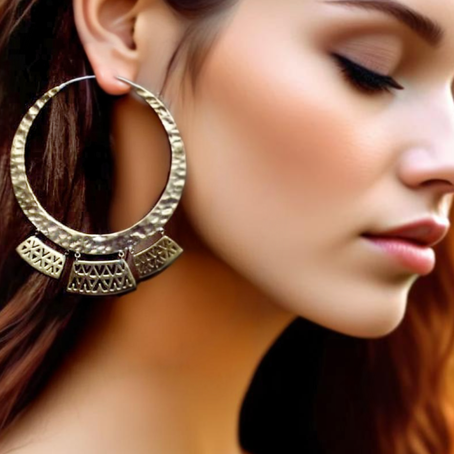 Model wearing large Italian brass Olteca earrings, with a hammered finish and intricate triangular motifs, styled against a rustic background.
